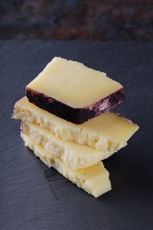 Hard cheese pieces on a dark background. Goat cheese on a slate board. Long ripening craft cheese....