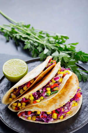 Vegetarian tacos with various vegetables, guacamole and lime on dark background. Tacos with sweet...
