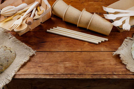 Different wooden kitchenware on wooden table. Wooden cutlery on old planks. Bamboo straws and disposable paper cups. Eco-friendly tableware. Zero waste concept. Top viewの写真素材