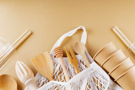Wooden cutlery and string bag on beige background. Disposable paper cups and glassware on earth...