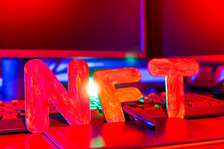 NFT (Non-Fungible Token) text of letters illuminated with neon light. Workplace of a graphic designer creating NFT digital art. Concept of cryptoart and blockchain technologyの写真素材