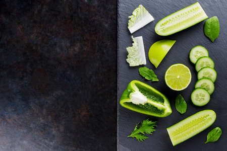 Different green fruits and vegetables on a dark background. Healthy vegetarian food on a slate board. Top view. Copy spaceの写真素材