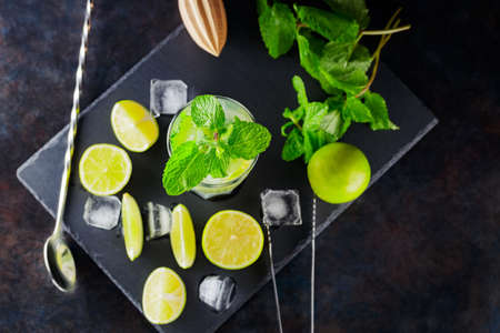 Mojito cocktail and ingredients on a dark background. Refreshing cocktail mojito on a slate board. Summer cocktail concept with lime and mint. Top viewの写真素材