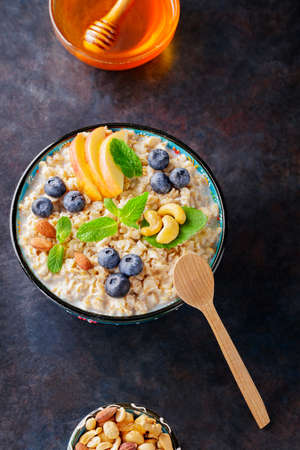 Bowl of oatmeal with blueberries, nuts and honey on a dark background. Oatmeal porridge with apple slices and fresh mint. Healthy food concept. top view. copy spaceの写真素材