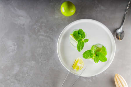 Mojito cocktail and bar accessories on gray background. Two highball glasses of mojito on a white plate. Summer refreshing cocktail with lime and mint. copy spaceの写真素材