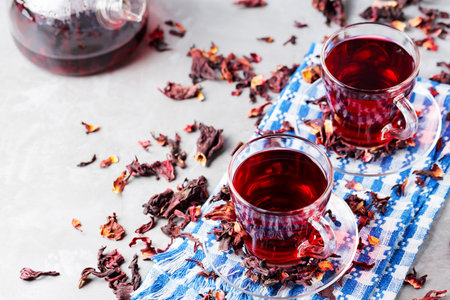 Two glass cups of hibiscus tea on a blue napkin. Hibiscus tea and dry hibiscus petals on a gray background. Healthy trending drink conceptの写真素材