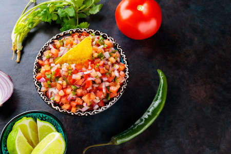 Pico de Gallo salsa and ingredients. Bowl of tasty Pico de Gallo salsa on dark background. Mexican food concept. top view. copy spaceの写真素材