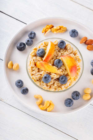 Bowl of oatmeal porridge with berries and slices of apples. Healthy breakfast with oatmeal, blueberries, apples and various nuts on white boards. top view. copy spaceの写真素材