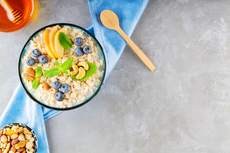 Oatmeal bowl with blueberry, nuts and honey on a gray background. Oatmeal porridge with apple and...
