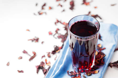 Hibiscus tea in a tall glass on a blue napkin. Healthy hibiscus tea and dry hibiscus petals on a white background. copy spaceの写真素材