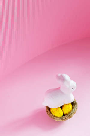 Easter eggs and rabbit on a pink background. Yellow golden eggs in a nest. Easter concept. copy spaceの写真素材
