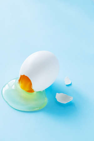Broken chicken egg on a blue background. Broken eggshell with liquids inside. Happy Easter concept....