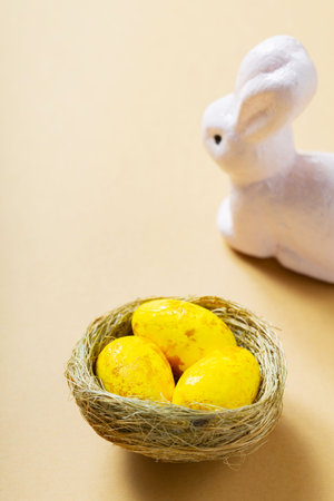 Yellow eggs and easter bunnies. Easter eggs in the nest on a beige background. Easter decoration concept. top view. copy spaceの写真素材