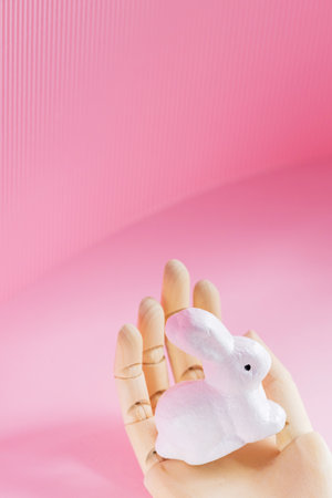Easter Bunny in a wooden hand. White rabbit in an artificial hand on a pink background. Futuristic Easter concept. opy spaceの写真素材