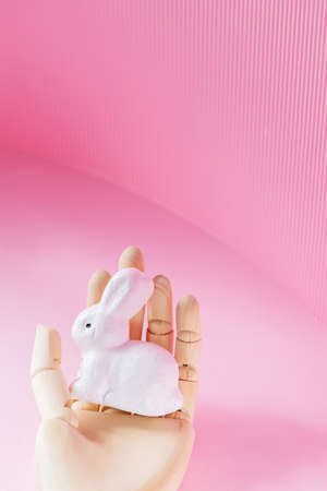 Easter Bunny in a wooden hand. White rabbit in an artificial hand on a pink background. Futuristic Easter concept. opy spaceの写真素材