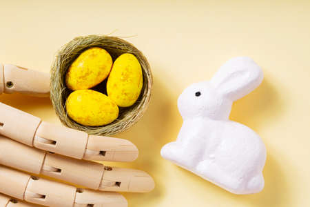 Easter eggs in an artificial arm. Yellow eggs in the nest and easter bunny on a pastel yellow...