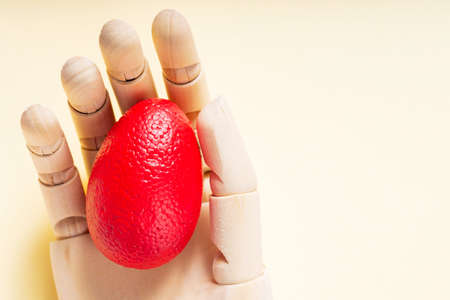 Red Easter egg in an artificial arm on a pastel yellow background. Surreal Easter concept. top view....