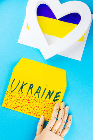 White heart on a blue-yellow background. Artificial hand holds an envelope with the inscription...