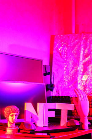 NFT (Non-Fungible Token) and computer equipment in pink neon light. NFT inscription with antique...