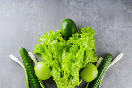 Green healthy vegetables on gray concrete. Fresh vegetables and fruits: lettuce, cucumbers, green onions, avocados, green apples. Healthy diet food concept. top view. copy spaceの写真素材