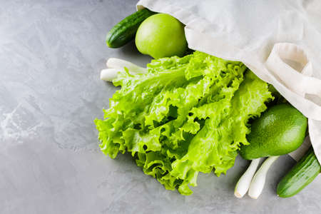 Green vegetables and fruits, greenery in shopping cotton bag. Eco linen bag with green fruits and vegetables on a gray background. Reasonable consumption concept. copy spaceの写真素材