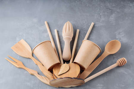 Reusable wooden kitchen utensils on gray background. Wooden kitchenware, bamboo straw and disposable...