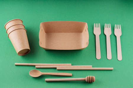 Eco-friendly tableware, paper disposable cup and wooden cutlery on a green background. Environmentally friendly disposable tableware, bamboo straws and forks. plastic free conceptの写真素材