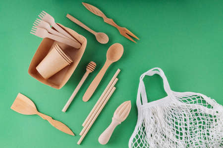 Wooden cutlery and shopping bag on a green background. Eco-friendly kitchen utensils, paper...