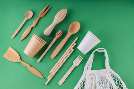 Eco-friendly kitchen utensils and mesh on a green background. Wooden cutlery, paper biodegradable tableware and shopping bag bag. Zero waste concept. top viewの写真素材