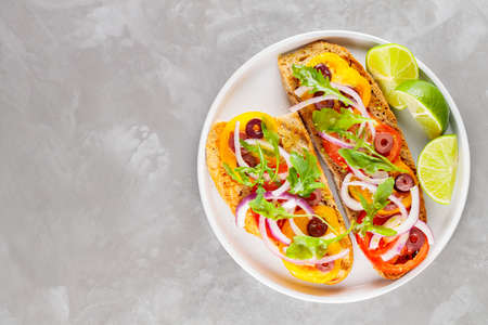 Healthy vegetarian toasts and lime on white plate. Bruschetta with tomatoes, greens and olives. Healthy open sandwiches on concrete. top view. copy spaceの写真素材