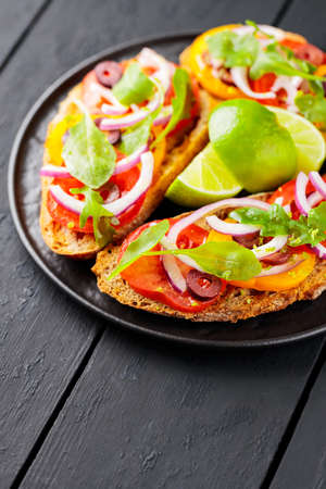 Healthy vegetarian toasts and lime on a black plate. Bruschetta with tomatoes, greens and olives....