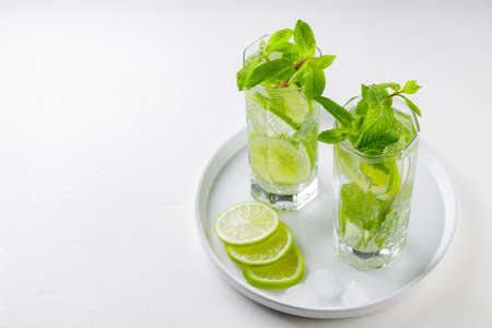 Mojito cocktail on a white background. Two glasses of mojito with mint and lime on a white plate. Summer drink concept. copy spaceの写真素材