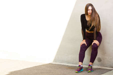 Young girl in sportswear is resting after running. Girl after exercise leaned against the wall on a sunny day. Healthy lifestyle concept. copy spaceの写真素材