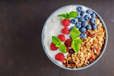 Granola with yogurt and berries on a dark brown background. Healthy breakfast with yogurt, baked...