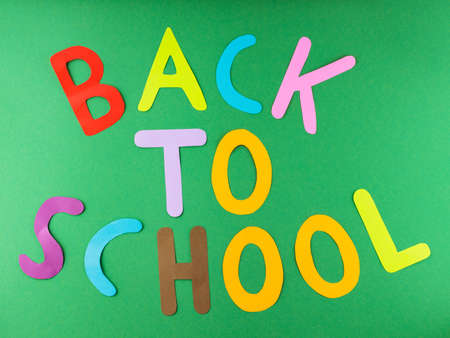 Inscription Back to school with multicolored paper letters. Back to school on a green background....