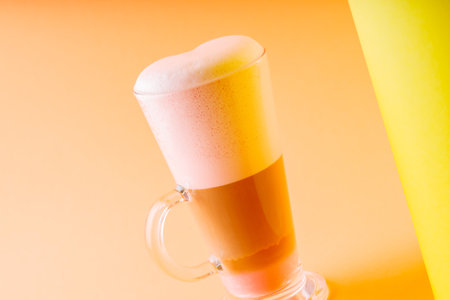 Latte macchiato coffee in tilted glass. Latte macchiato with pink foam on coral yellow background. Creative concept of coffee drink with milkの写真素材