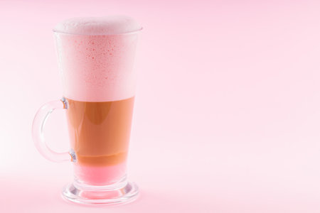 Latte macchiato with pink foam on a pink background. Latte macchiato coffee in a transparent glass....