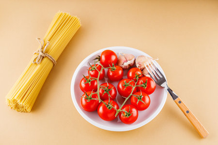 Pasta spaghetti with tomatoes and garlic on a beige background. Raw pasta and fresh vegetables. top viewの写真素材