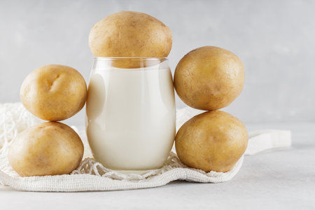 Alternative potato milk in glass and potatoes. Alternative non dairy drink and string bag. Vegan potato milk and sustainable lifestyle conceptの写真素材