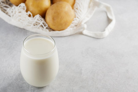 Potato milk and raw potatoes in a mesh bag. Alternative non dairy drink and ingredients on gray background. Allergens free and zero waste concept. top view. copy spaceの写真素材