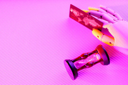 Bank card in an artificial hand. Credit card and hourglass in neon light. Time is money concept....