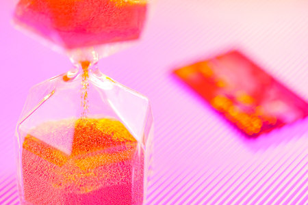 Bank card and hourglass on a purple background. Sandglass and credit card in neon light. Time is...