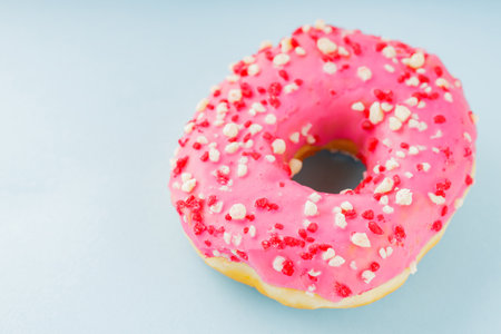Donut with icing on pastel blue background. Pink donut with colorful toppings. copy spaceの写真素材