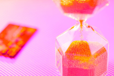 Bank card and hourglass on a purple background. Sandglass and credit card in neon light. Time is money conceptの写真素材