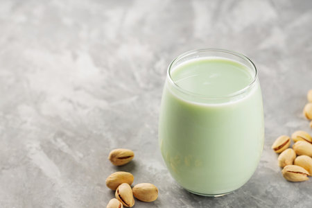 Organic non dairy pistachio milk in glass with pistachionuts on gray background. Vegan plant based milk. copy spaceの写真素材