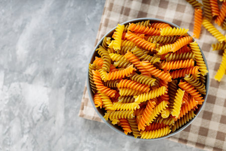 Dry pasta in a bowl on a gray background. Three colors fusilli pasta on a linen napkin. copy spaceの写真素材