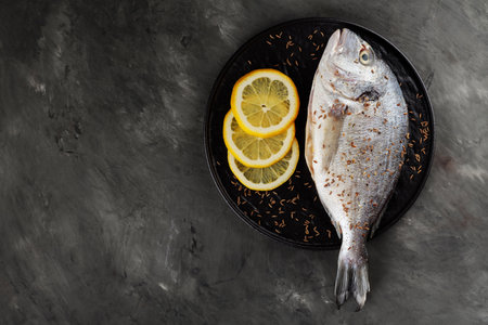 Fresh raw dorado fish and lemon slices on dark background. Top view. Copy space