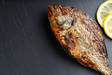 Whole baked dorado fish lemon slices on slate board. Copy space