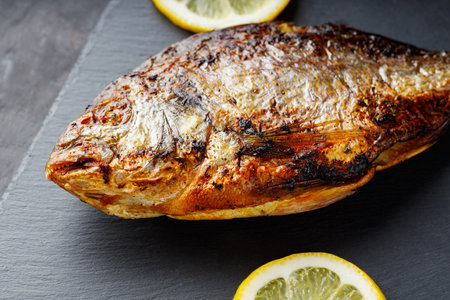 Fried dorado fish with lemon on dark background. Close up