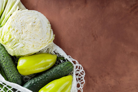 Fresh Green Vegetables in Mesh Bag on Brown Clay Background, Copy Space, Top View